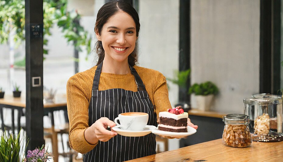 Eine junge Dame reicht Kaffee und zusätzlich Kuchen als Teil der eigenen X-Sell-Strategie 